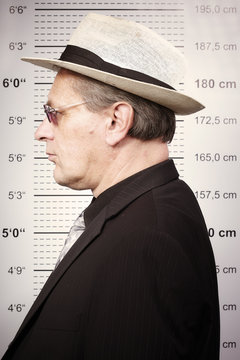 Criminal man portraited in sunglasses and hat in front of mug board