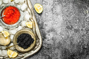 Black and red caviar in bowls on old tray.