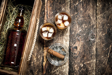 Whiskey background. A bottle of whiskey in an old box with glasses and a cigar.