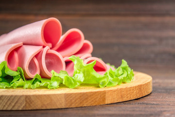 Sliced sausages with salad leaves on the wood background.