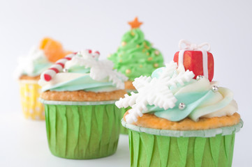 New year or christmas greencupcakes with whipped cream, decorated with a christmas tree, candy cane, a snowflake, a gift, tangerines, silver and gold confectionery balls on white background.