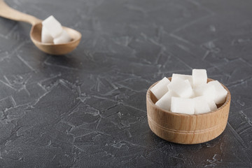 pieces of sugar in  bowl and spoon on  dark background