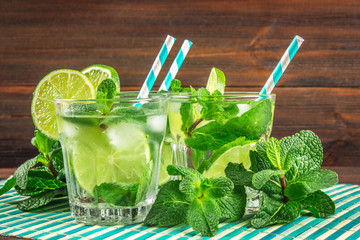 Mojito with mint and lime in a glass and a jug on the round board. Brown wood background