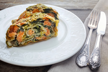 Strudel pie with salmon and spinach, served on wood table