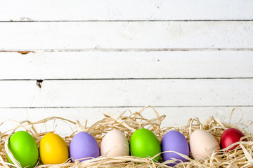 Easter eggs in nest on wooden background, white boards with group of eggs in straw