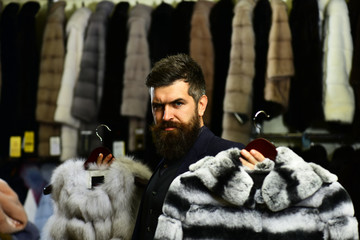 Customer with beard presents furry coats. Businessman with expensive overcoats