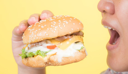 Woman eating tasty hamburger against yellow background,Close up