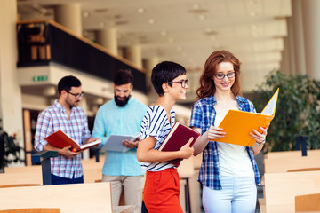 Happy young university students studying with books in library