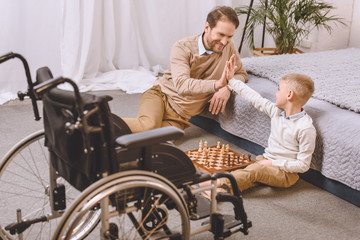 father with disability and son playing chess and giving high five