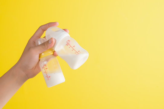 Hand Holding Two Baby Bottle Of Milk On Yellow Background