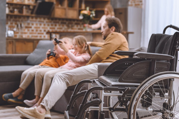 father looking how children playing video game with wheelchair on foreground