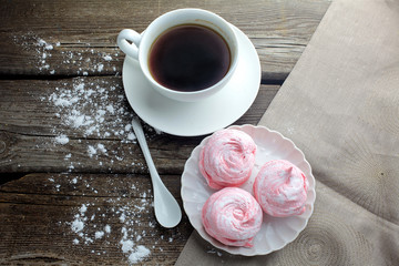 white ceramic cup with black coffee and marshmallow dessert on wooden table, top view