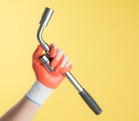 Wheel wrench in hand with gloves against yellow background