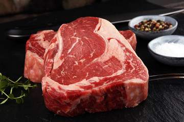 Raw fresh meat Ribeye Steak, seasoning and meat fork on dark background