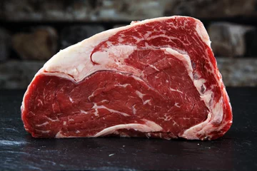 Crédence de cuisine en verre imprimé Viande Viande fraîche crue Ribeye Steak, assaisonnement et fourchette à viande sur fond sombre