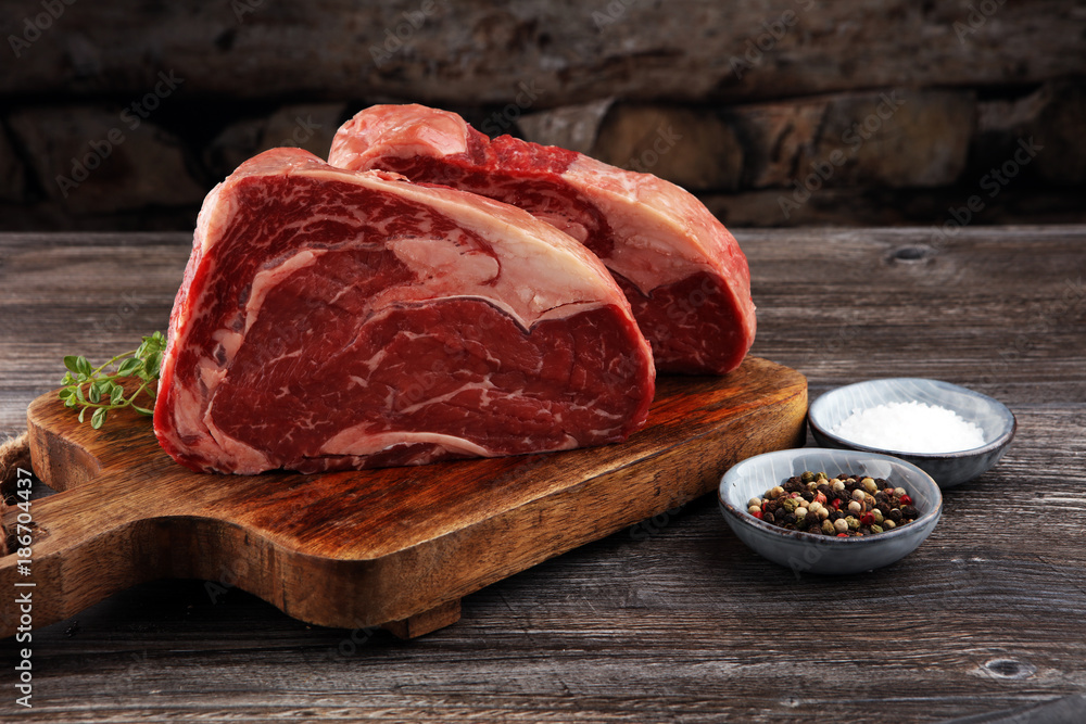 Wall mural raw fresh meat ribeye steak, seasoning and meat fork on dark background