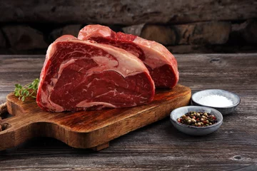 Crédence de cuisine en verre imprimé Viande Viande fraîche crue Ribeye Steak, assaisonnement et fourchette à viande sur fond sombre