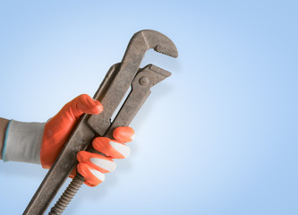 Handyman hand with glove holding pipe wrench on blue background