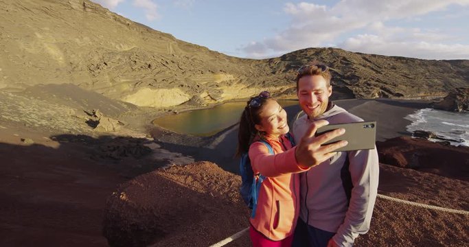Couple taking selfie video using mobile smart phone hiking in volcano mountains on tourist travel in Lanzarote, Canary island, Spain. Lago Verde volcanic green lake. RED EPIC SLOW MOTION.