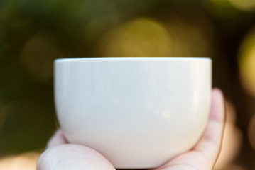 Woman hand holding a cup of coffee in the morning, with nature background. Relaxing and healthy concept.