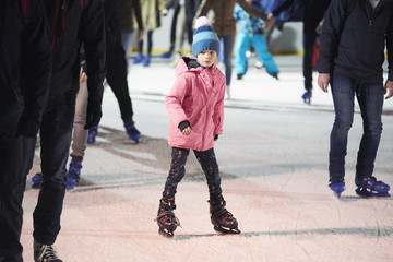 Child young girl ice skating at the ice rink outdoors. Child learning to skate on public rink.  Ice skaters using a temporary rink during the Christmas and New Year holiday period - obrazy, fototapety, plakaty