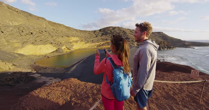 People taking photo using mobile phone in volcano mountains of Lanzarote, Lago Verde volcanic lake, El Golfo. Lanzarote. Canary Islands. Spain. Taking smartphone photo. RED EPIC SLOW MOTION.
