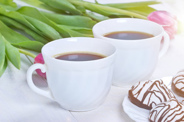 Two cups of coffee with pink tulip on white background