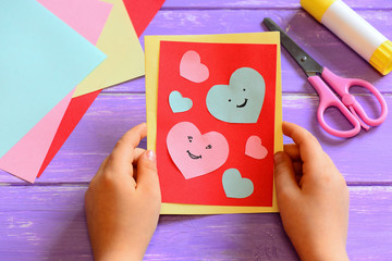 Child is holding a Valentines greeting card in his hands. Child is showing a Valentines greeting...