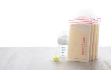 Breast milk frozen in storage bags with baby bottle on table wood