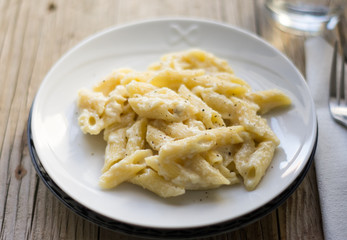 Homemade italian four cheese pasta on a white plate on a wooden table