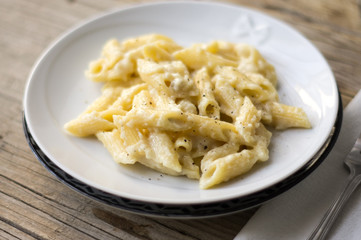 Homemade italian four cheese pasta on a white plate on a wooden table