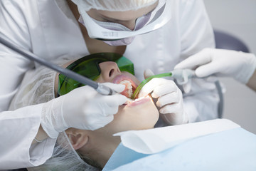 Naklejka premium Young female patient visiting dentist office.Beautiful woman with healthy straight white teeth sitting at dental chair with open mouth during a dental procedure.Dental clinic. Dental caries
