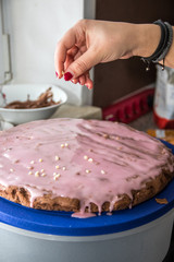 Frau mit rotlackierten Fingernägeln streut Mandeln auf Kuchenglasur in der Küche