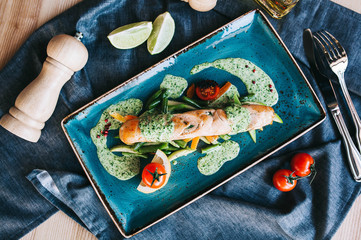 Fototapeta na wymiar roll of red fish with spinach with vegetables, bell pepper and, asparagus beans and cherry tomatoes on a blue plate