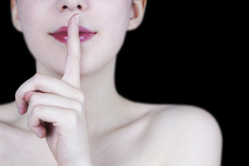Naklejka premium Close up of young woman's face smiling with red lips showing silence gesture on black background - secret concept