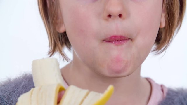 A young girl enjoys eating a banana and she gives thumbs up.