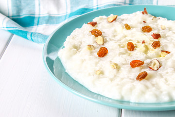 Rice milk porridge with nuts and raisins in a blue dish on a white wooden table.