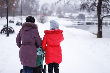 Woman with an adult daughter and a stroller on a walk in winter park