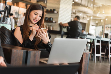 Beautiful asian woman in black dress working with laptop taking note in coffeeshop