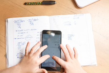 Schoolboy with smartphone doing homework at home.