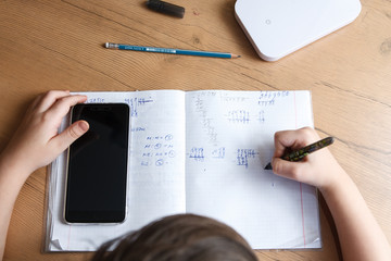 Schoolboy with smartphone doing homework at home.