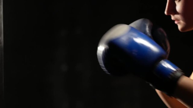 Strong woman fighter in boxing gloves on hands beating punching bag