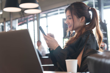Fototapeta premium Beautiful asian woman in black dress working with laptop and smartphone in coffeeshop