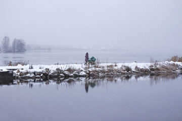 Young mother walking with stroller near lake in winter