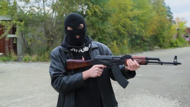 Terrorist holding kalashnikov rifle. Masked man holding a Kalashnikov rifle, takes aim and shoots. Criminal with a gun in the hands