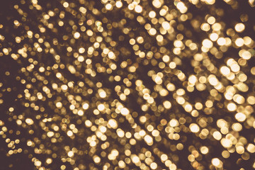 Background image of gold color bokeh against dark background generated by diffused and defocused real lights