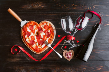 a festive dinner of pizza in the shape of a heart and a bottle of wine.