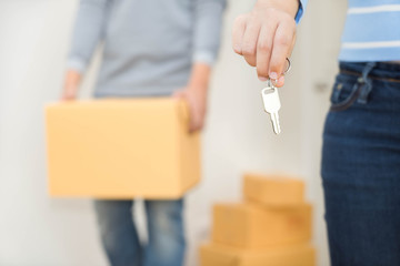 Close up of hand holding a key while a man holding a box to move in - buying new house concept.