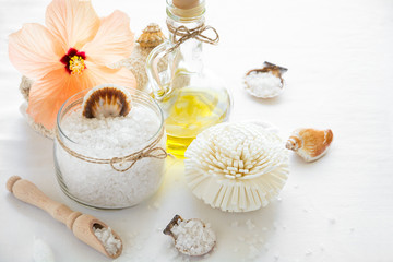 Fototapeta na wymiar Wellness setting. Sea salt in glass, soap, towel, olive oil and flowers on white textured background. Space for copy. Flat lay