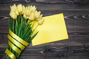 Spring background with bouquet of yellow tulip flowers and blank sheet of paper, copy space. Flat lay, top view. Holiday greeting card for Valentine's Day, Woman's Day (March 8, Mother's Day, Easter